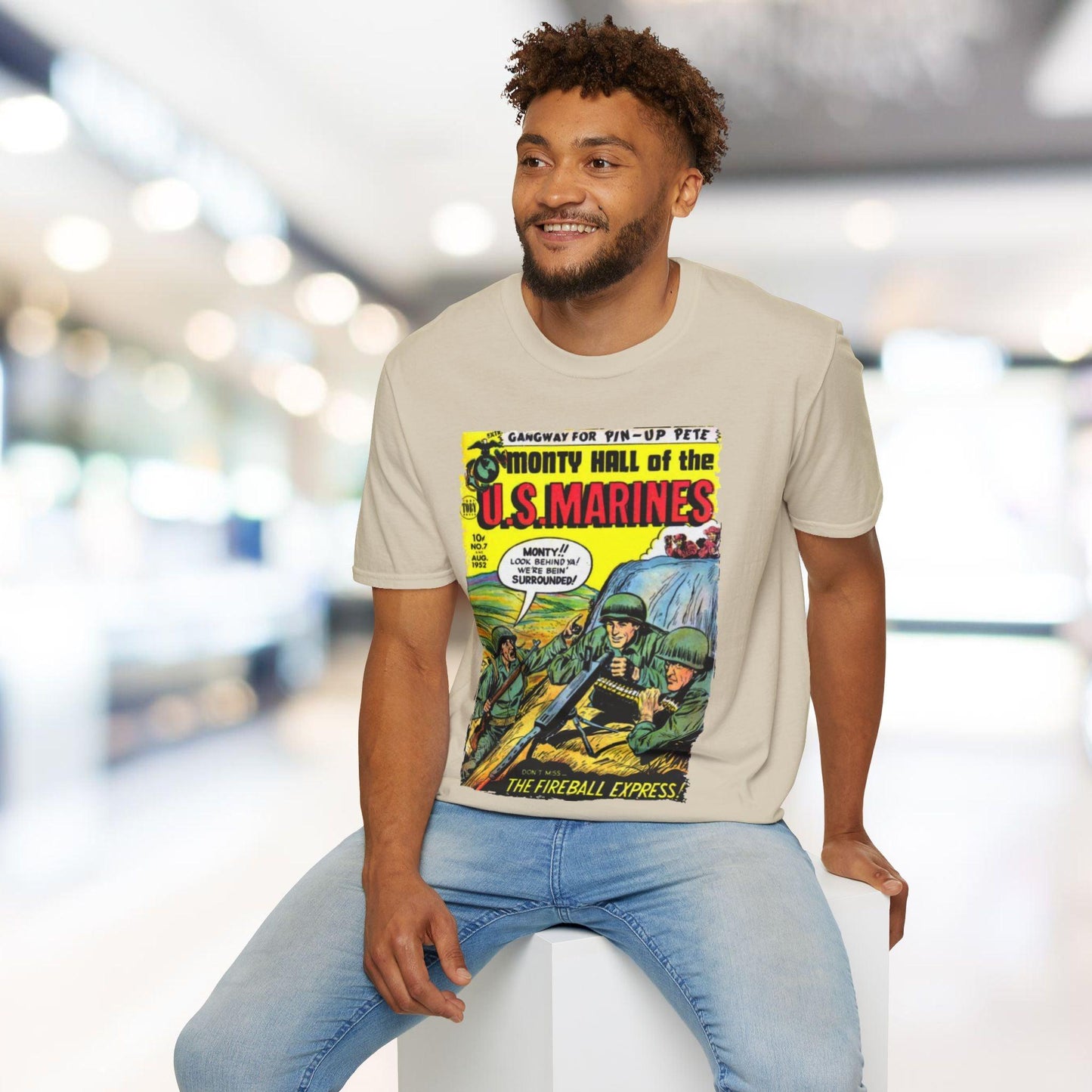 Man wearing a t-shirt with a comic book graphic design, sitting in a modern indoor setting.